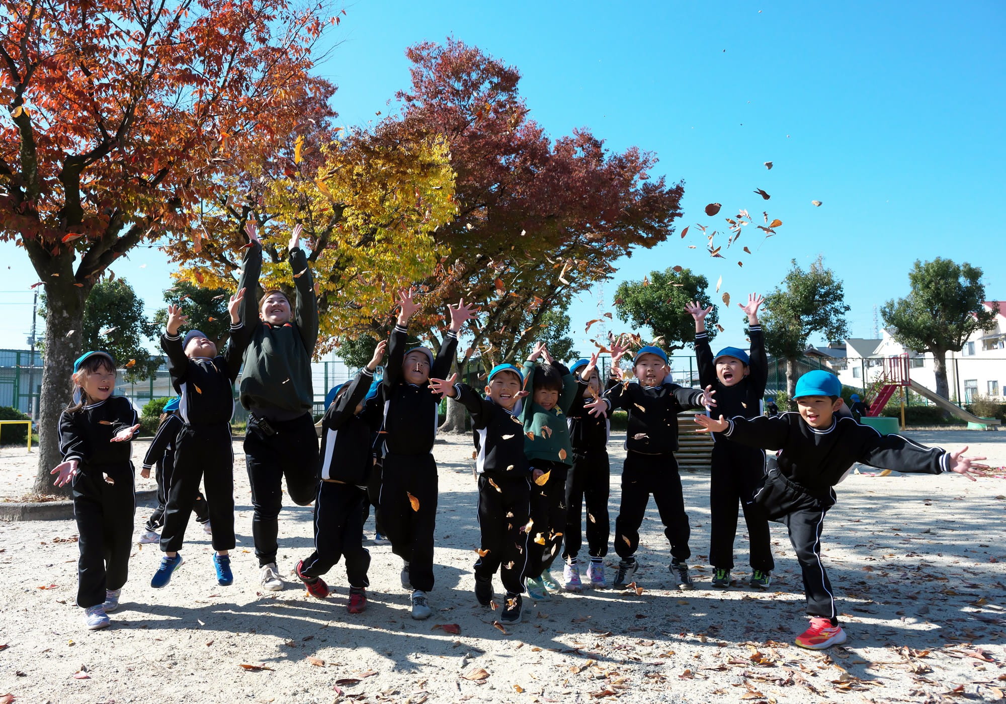 落ち葉であそぶ保育士と園児たち